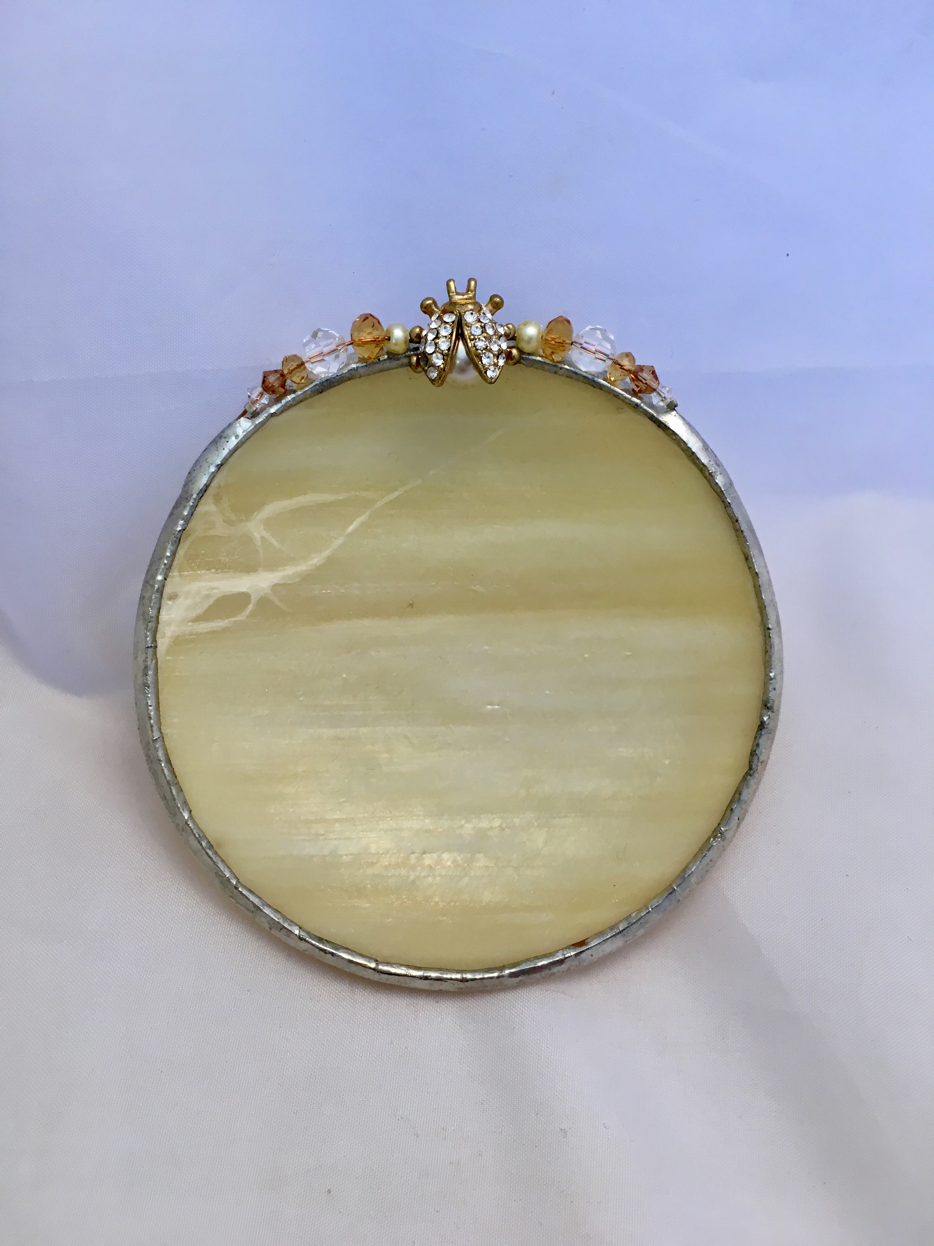 A round mirror with a decorative frame on top.