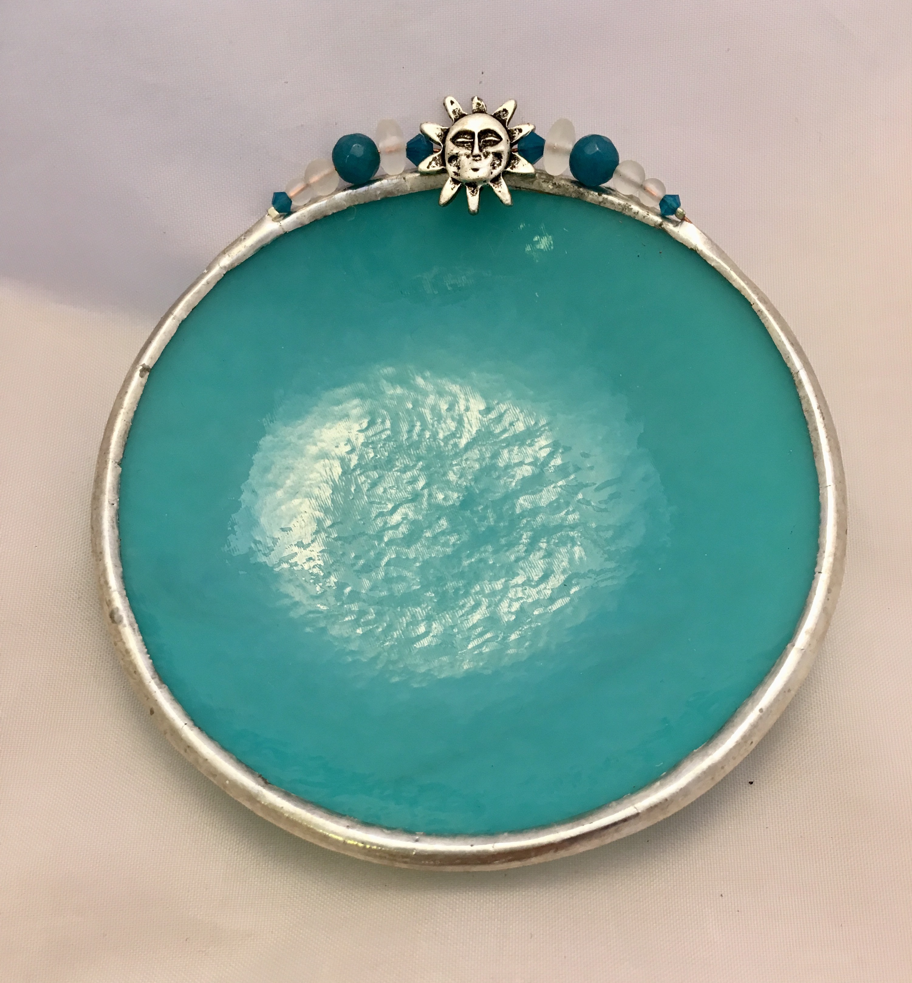 A turquoise plate with silver rim and face on top.