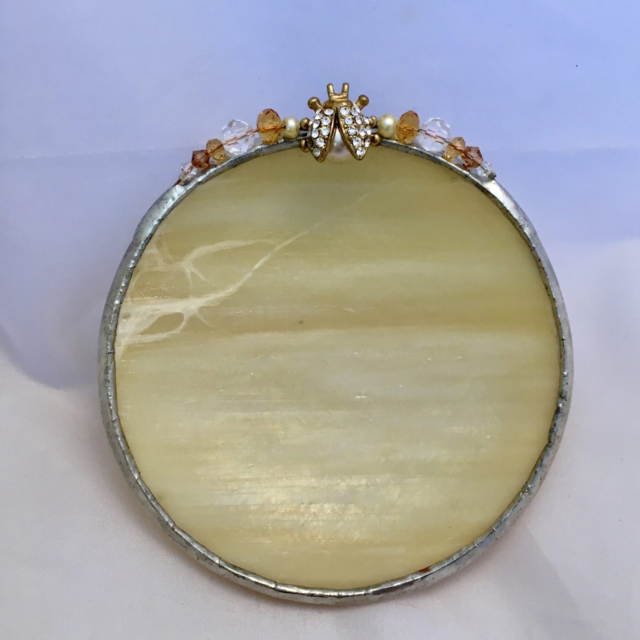 A round picture frame with a yellow stone and gold trim.