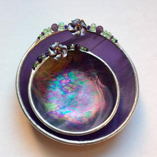 A purple bowl with a silver rim and some green beads