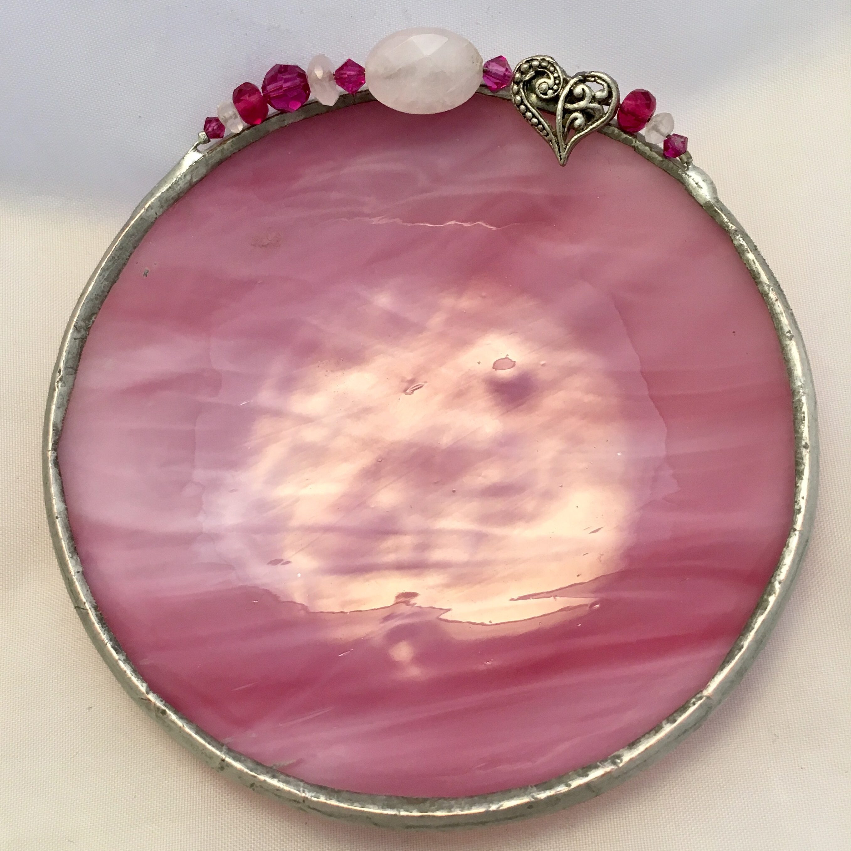 A pink stained glass circle with a bead and flower on it.