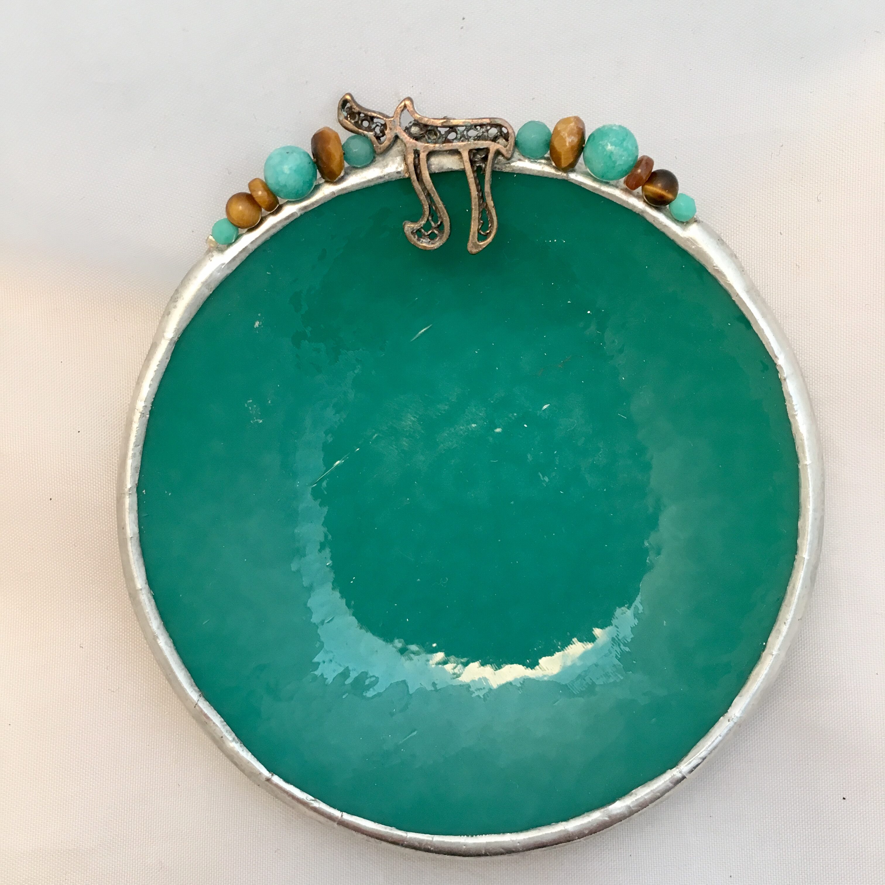 A green bowl with beads and a silver rim.